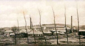 L’usine vue de la rivière. Entre les deux hautes cheminées, l’ensemble des bâtiments.